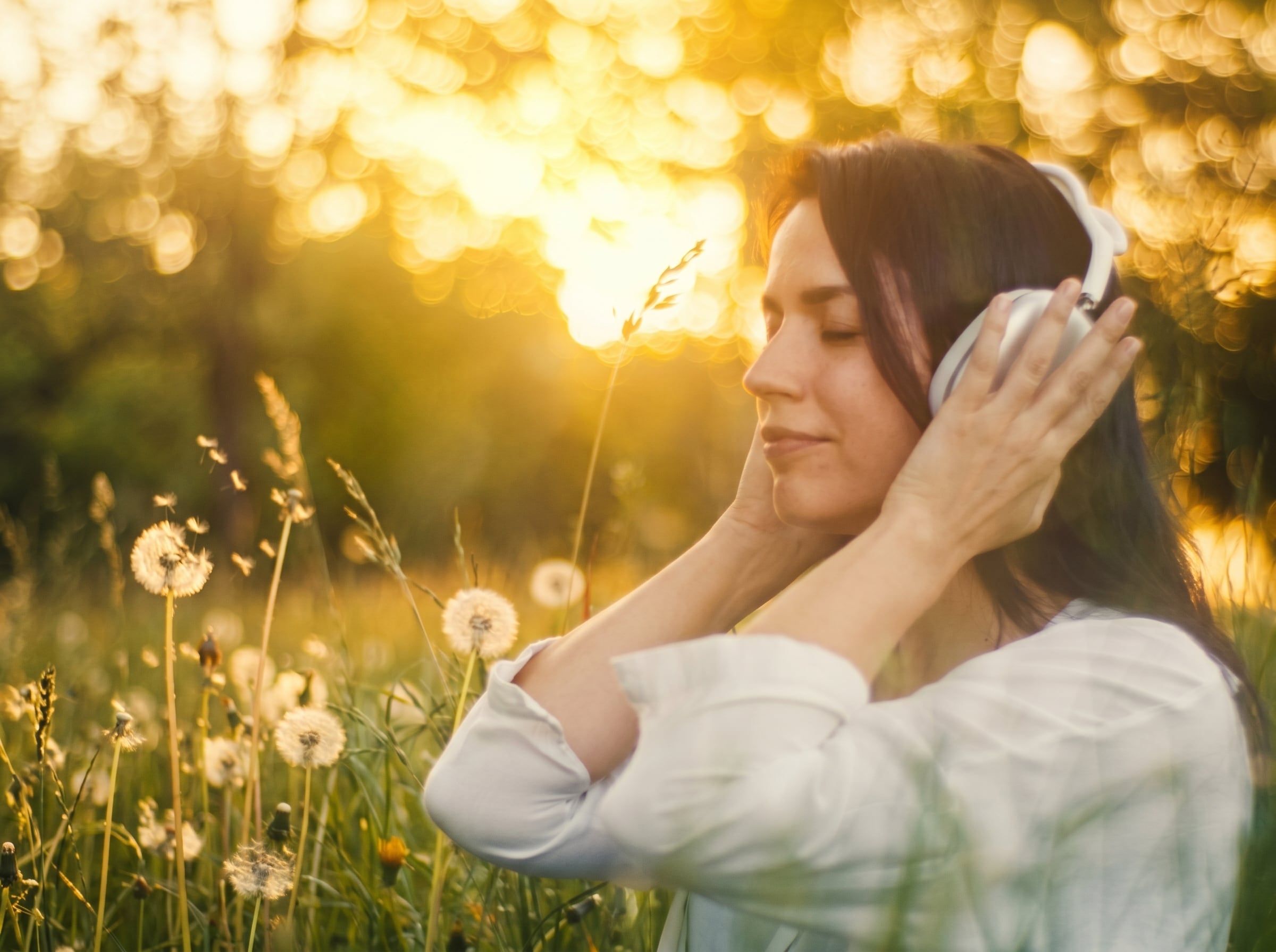 A woman listening with her eyes closed in a sunlit meadow, wearing the Lautsänger Challenge