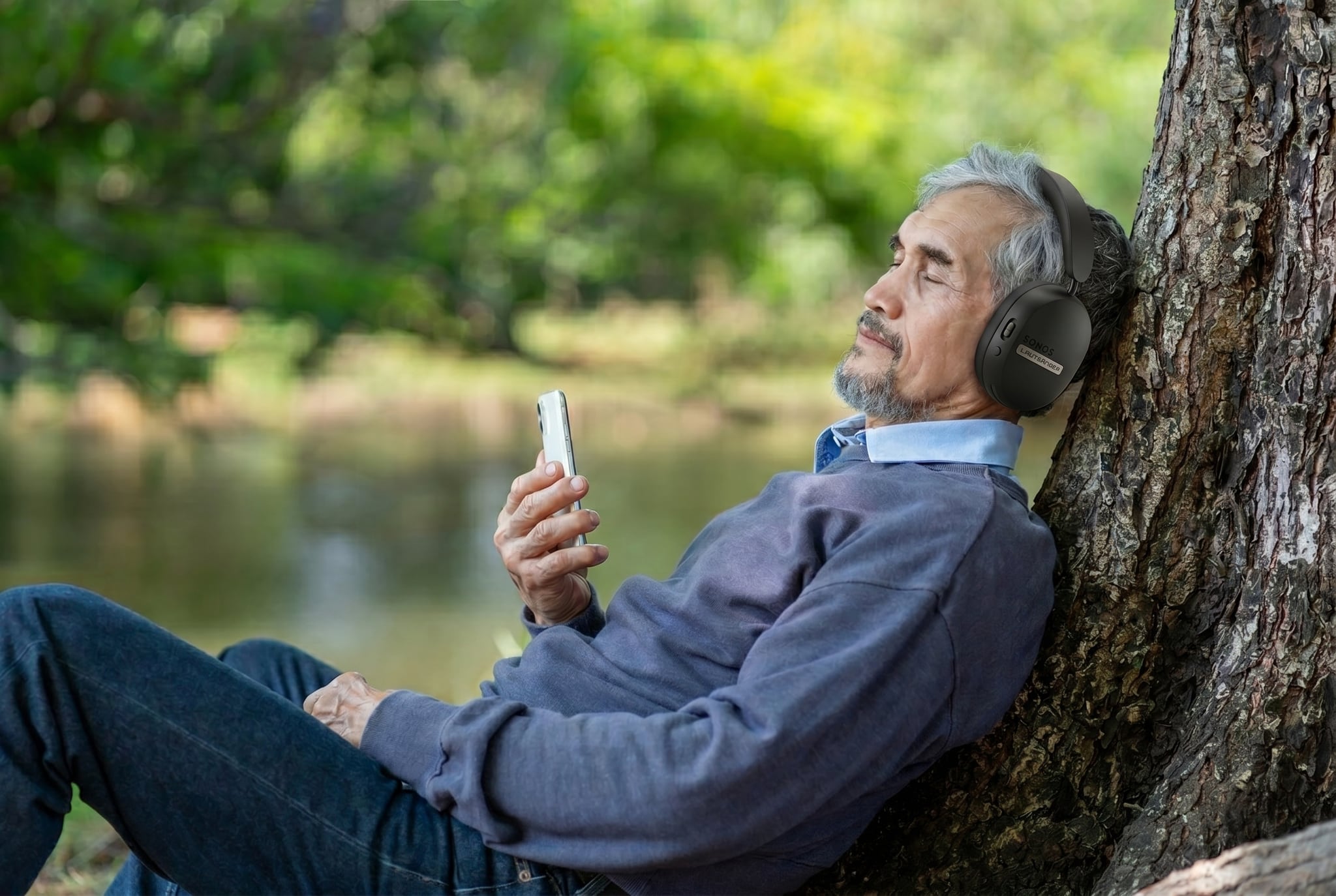 A listener at rest against a tree by the water, eyes closed, wearing the matte-black Lautsänger Challenge